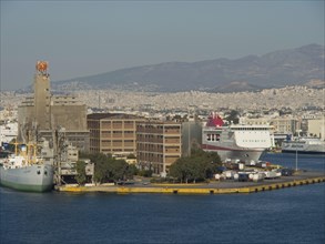 Harbour with large ships and buildings, behind it a cityscape with mountains in the background,