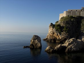 Rocks and coastal fortress on the calm sea under a clear blue sky, the old town of Dubrovnik with