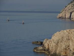 Two boats sail on the calm sea along a rocky coast, the old town of Dubrovnik with historic houses,