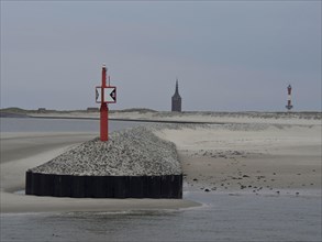 Red beacon on gravel embankment, divided coastal landscape with sand dunes and church tower in the