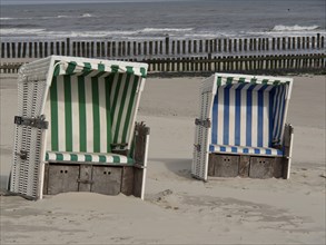 Two beach chairs, one green and white and the other blue and white striped, in front of a calm sea