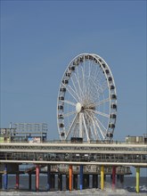 Ferris wheel on a pier reaching into the sea under a blue sky, parasols and a pier on the beach of