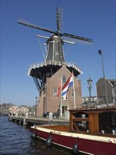 A traditional windmill with a Dutch house in the foreground, next to a quiet canal, Haarlem,