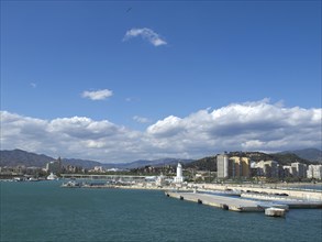 Panoramic view of a harbour with buildings, mountains in the background and cloudy blue sky, the