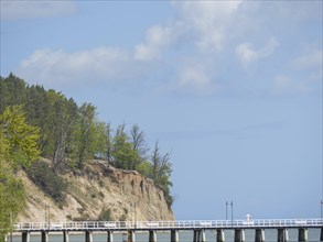A long bridge stretches along high cliffs and flows into the sea, spring on the Baltic Sea beach in