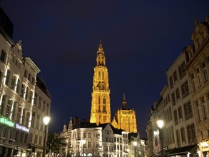 An imposing, illuminated church tower dominates the scenery of a lively city at night, Historic