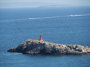 Small red lighthouse stands on a rock in the blue sea, boats in the background, ibiza, Spain,