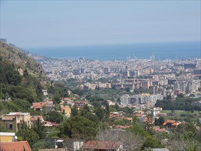 A sweeping panorama of a city with houses, green hills and the sea in the background, palermo in