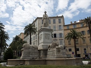 Historical monument with a statue and lions in an urban setting, surrounded by palm trees and
