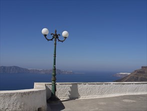 Street lamp on a white terrace with a view of the sea and mountains in the background, The volcanic