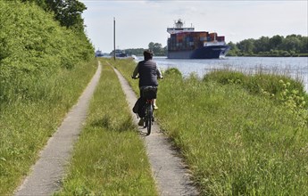 Cycling with a container ship on the Kiel Canal, Kiel Canal, Schleswig-Holstein, Germany, Europe