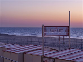 A sign with the inscription 'Sunset Beach' above the beach huts at sunset, sunset in many colours