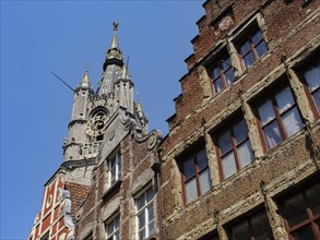 A clock tower and brick houses with ornate details under a clear blue sky, medieval facades with