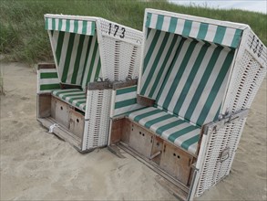 Two green and white striped beach chairs on the beach in front of a grass dune, Baltrum Germany