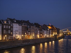 Townhouses along a river at night, illuminated windows reflected in the water, calm atmosphere,