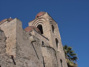 Historic church building with round towers, flanked by palm trees, under a clear blue sky, palermo