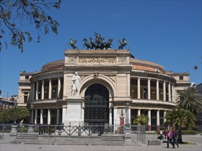 A large, round historical building with a statue and columns on a sunny square, palermo in sicily