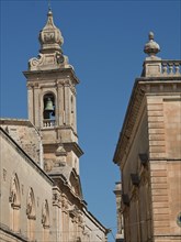 A tower with bell and adjoining building under a blue sky, the town of mdina on the island of malta
