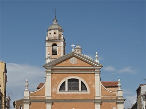 A historic church with two high towers and a decorative cross against a clear blue sky, Corsica,