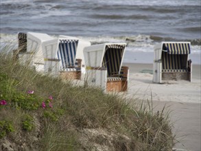 White beach chairs with blue and white stripes stand near the dunes by the sea with waves, beach