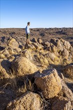 Young man on rocks, barren landscape with rocky hills and acacia trees, African savannah in the