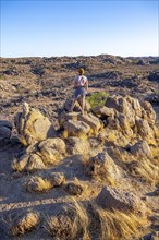Young woman on rocks, barren landscape with rocky hills and acacia trees, African savannah in the