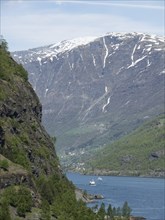 A picturesque river surrounded by snow-capped mountains with moving boats, spring by a fjord with