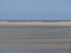Empty beach at low tide with strips of sand and water under a blue sky, Baltrum Germany