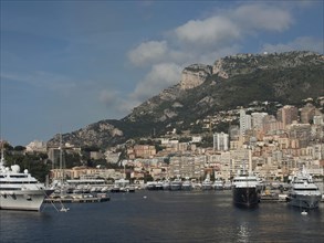 Harbour city with many high-rise buildings on the coast, with yachts in the water and mountains in