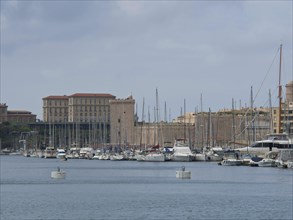 A harbour full of boats and yachts with historic buildings and sailing masts in the background,