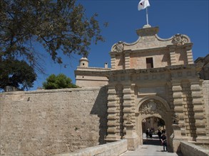Large sandstone city gate with visitor access and historic charm under a blue sky, the town of