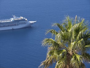 Cruise ship in tropical sea with a palm tree in the foreground and blue sky, The volcanic island of