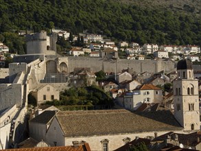 Historic city wall and fortress in the foreground, with mediterranean houses and mountains in the