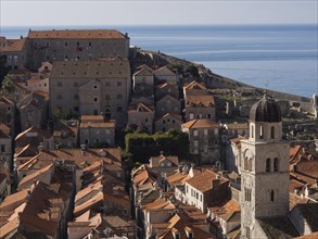 Historic coastal town with tiled roofs and a church tower stretching along the coast, overlooking