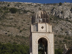 Stone bell tower against a backdrop of mountains and vegetation under a clear sky, the old town of