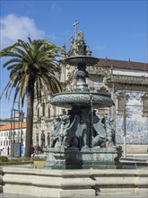Ornamental fountain with mythological figures, large palm tree and baroque church in the