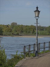 View of a river with an old lantern and green bank in spring, rhine promenade of Rees with historic