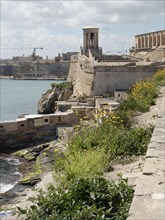 Coastal view of an old town with flowers and wall by the sea, blue sky with clouds, Valetta, Malta,