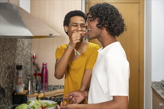 Romantic gay man feeding his couple in the kitchen with a tomato cherry