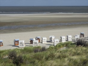 Several beach chairs on a quiet beach with grass and sweeping views of the sea and sky, Spiekeroog,