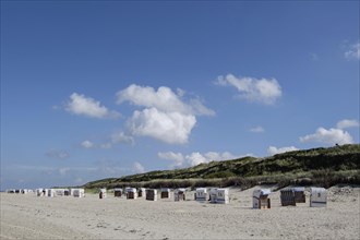 Beach with many beach chairs, grassy dunes and blue sky with clouds in the background, Spiekeroog,