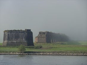 A partially dilapidated ruin in a green landscape, shrouded in fog, fog at the rhine river with an
