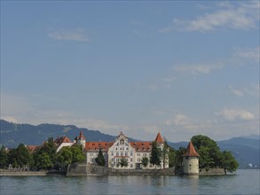 A castle with red roofs on a lake, surrounded by trees and mountains in the background, view of a