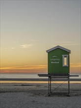 Sunset over the sea with green lifeguard tower on the beach, setting sun on the North Sea beach