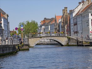 Canal with stone bridge and colourful flowers, flanked by historic houses and lively city life on a