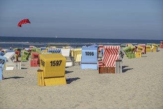 Colourful beach chairs on the sandy beach, a red kite flying, calm sea scenery under a clear sky,
