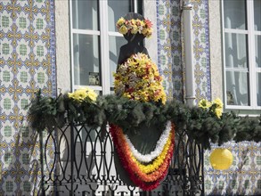 Colourful floral decoration on an ornate balcony with statue and tiles in the background, Lisbon,