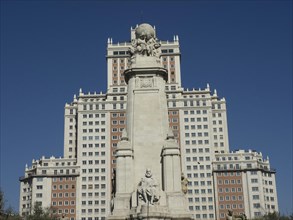 Large monument with sculptures in front of an imposing skyscraper under a clear sky, Madrid, Spain,