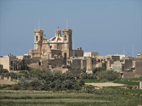 A church with red domes and twin towers dominates the cityscape, the island of Gozo with historic