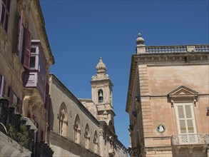 Historic buildings under a blue sky with a church tower in the background, the town of mdina on the